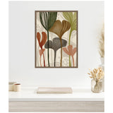 Framed canvas wall art featuring abstract botanical shapes in earthy tones of green, brown, and terracotta with a beige background hanging above a minimalist desk with dried floral decor.