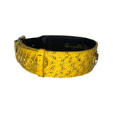 Mustard yellow dog collar with black snake scale texture and metal buckle, shown in a circular shape on a white background.