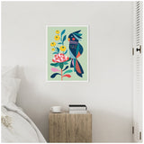 Framed colorful abstract cockatoo perched beside stylized pink and yellow flowers on pale green background, hung on white wall above wooden bedside table with books and cup.