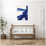 Abstract wall art with bold cobalt blue brushstrokes on white canvas, hung above a wooden bench with white cushions in a minimalistic room.