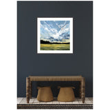 Square framed painting depicting a dramatic sky with swirling clouds above a horizon of dark tree silhouettes and green fields, mounted on a dark gray wall above a rustic wooden bench with woven seats.