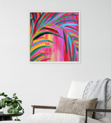 Abstract colorful painting featuring bold, curved strokes in pink, green, yellow, and blue tones, framed and hanging on a white wall above a modern armchair with a gray throw.