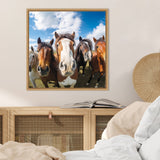 Close-up of five horses with curious expressions standing in a row under a partly cloudy blue sky, framed in wood on a beige wall above a light wood cabinet.