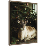 Framed canvas art of a reindeer sitting under a decorated Christmas tree in soft light