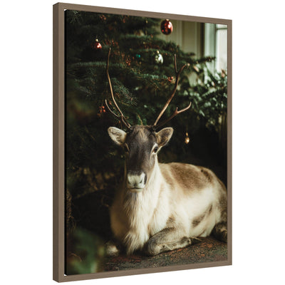 Framed canvas art of a reindeer sitting under a decorated Christmas tree in soft light