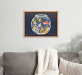 Framed illustration of a goldfish swimming among pink and yellow aquatic plants inside a round fishbowl on a dark blue background, displayed above a gray sofa with cream blanket.