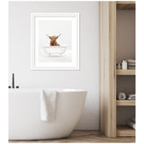 White solo bathtub with a towel on its edge in a minimalist bathroom, framed print above shows a brown Highland cow peeking over a white clawfoot tub.
