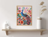 Framed colorful art print of a stylized blue peacock with elaborate multicolored tail feathers, surrounded by large pink and orange flowers, displayed on a wall above a wooden shelf with white vases and tall beige pampas grass.