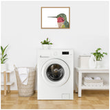 Framed canvas print of a colorful hummingbird with a green head and red throat, hanging on a white wall above a white front-loading washing machine.
