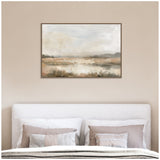 Framed abstract landscape artwork above a bed with white and beige pillows, featuring soft neutral tones and blurred natural elements in beige, brown, and gray hues.