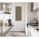 Tall narrow framed botanical block print with green background and white leaf patterns hanging on a white wall in a modern kitchen with gray countertops and light tile flooring.