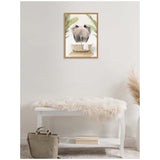 Framed canvas print of an elephant's backside above a white clawfoot bathtub with palm leaves, hanging on a plain light-colored wall above a white bench with a faux fur throw.
