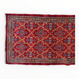 Vintage red Mashhad wool runner featuring intricate floral and geometric patterns in blue, ivory, and black with a detailed border, shown flat from above.