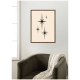 Minimalist framed wall art featuring three black starburst shapes on a beige background above a dark green armchair with a cream knitted blanket draped over it.