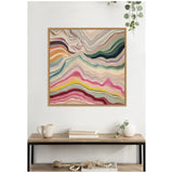 Framed square canvas with abstract layered waves in beige, pink, yellow, green, purple, and red tones, hanging above a wooden shelf with decor items.