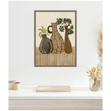 Framed canvas print of three stylized vases with green foliage on a beige background and brown vertical stripes on lower half, hanging on a white wall above a light wood desk.