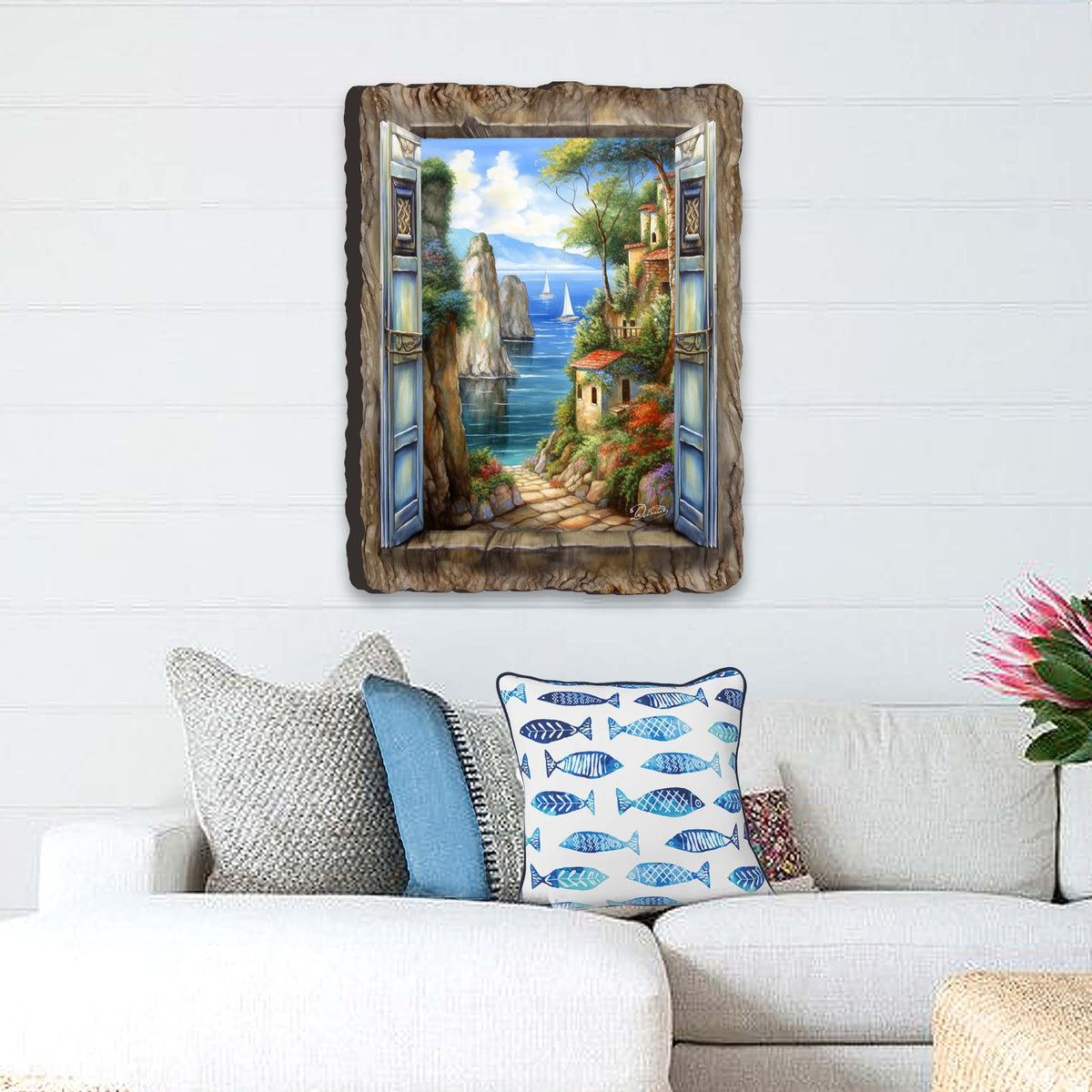 Wall art depicting a coastal village with blue-shuttered window frame, sailboats on blue water, and stone path surrounded by greenery and colorful houses.