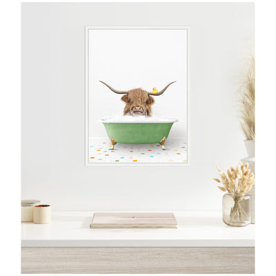 Framed canvas showing a Highland cow's head and horns emerging from a green clawfoot bathtub filled with bubbles, a yellow rubber duck on its head, colorful tiled floor below.