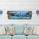 Wooden wall art with rough natural edges depicting a glacier with blue ice and snow-capped mountains, mounted above a light blue sofa with coral-patterned pillows.