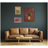 Three framed floral and still life prints on a dark green wall above a tan leather sofa with a wooden coffee table holding a glass vase and candles