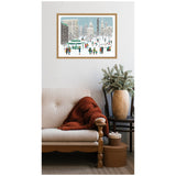 Framed canvas artwork showing a snowy urban park with people walking and buildings in the background, hung above a beige sofa and a wooden chair with a potted plant.