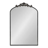 Arched mirror with a simple black frame topped by an ornate scrollwork floral design in dark bronze tone, blending traditional and elegant styles.
