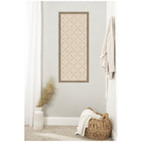 Vertical rectangular light beige textile artwork with a subtle green lattice pattern framed in wood, hanging on a pale gray wall between white curtain and wicker basket with white throw.