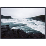 Framed canvas showing a turbulent waterfall with foamy white water flowing over dark rocky terrain under a cloudy gray sky.