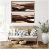 Two rectangular abstract art canvases in brown and beige tones, hung vertically above a light wooden bench with gray and white checkered pillows, surrounded by natural decor.
