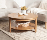 Round wood coffee table with a lower shelf holding a woven basket and blanket, topped with a white ceramic vase and small bowls, set on a patterned rug
