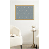 Wall-mounted pinboard with a muted blue fabric featuring a subtle repeating white botanical pattern, framed in light wood above a brass side table and cream armchairs.