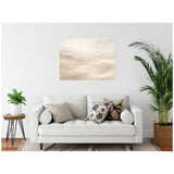 Abstract tonal framed canvas with white and beige textural patterns hanging above a white couch with patterned pillows, flanked by green plants on either side.