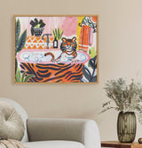 Framed colorful print of a tiger relaxing in a bubble bath with plants and patterned towels in a pink and orange bathroom scene, hung above a gray sofa.