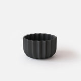 Matte black round planter with vertical ridges creating a wavy pattern on the exterior, shown isolated against a white background.