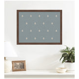 Wood-framed pinboard with blue fabric and small, evenly spaced white botanical block print motifs, hanging above a white shelf with decorative objects and a plant.