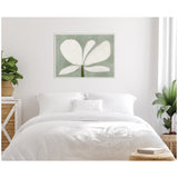 Minimalist bedroom with white bedding, featuring a wall art print of large white floral petals on muted green background, complemented by green leafy plants on sides.