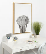Black and white framed canvas print of an elephant head with detailed wrinkles, displayed above a white desk with gold and green accents in a minimalist space.