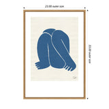 Minimalist blue figure curled forward with bent knees and arms extending to feet on cream background, framed in light wood with outer dimensions marked