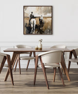 Square canvas artwork depicting two cowboys on horseback in an abstract neutral-toned painting, hung on a white wall above a wooden dining table with cream chairs.