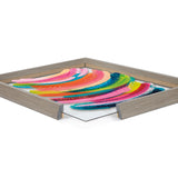 Colorful abstract curved brushstrokes in pink, yellow, blue, green, and orange on a white background within a light wood frame with a corner cutaway showing clear glass.
