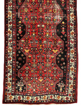 Vintage Persian Hosseinabad runner rug with red geometric medallions on a dark background, framed by a cream border featuring floral motifs in multiple colors.