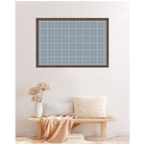 Rectangular wall-mounted pinboard with light blue and white plaid fabric inside a dark brown frame above a wooden bench with cream pillows, a beige throw, and a white vase with dried flowers.