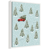 Sylvie Framed Canvas depicting a red car carrying a Christmas tree through a snowy forest with tall snow-covered trees and gentle snowfall.