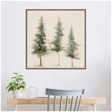 Framed canvas with abstract painting of three evergreen trees in green and earthy tones on a neutral linen background, hanging above a wooden desk with a plant and decor.
