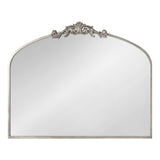 Large arched mirror with a silver frame and an ornate decorative silver crest at the top center featuring carved floral and scroll motifs.