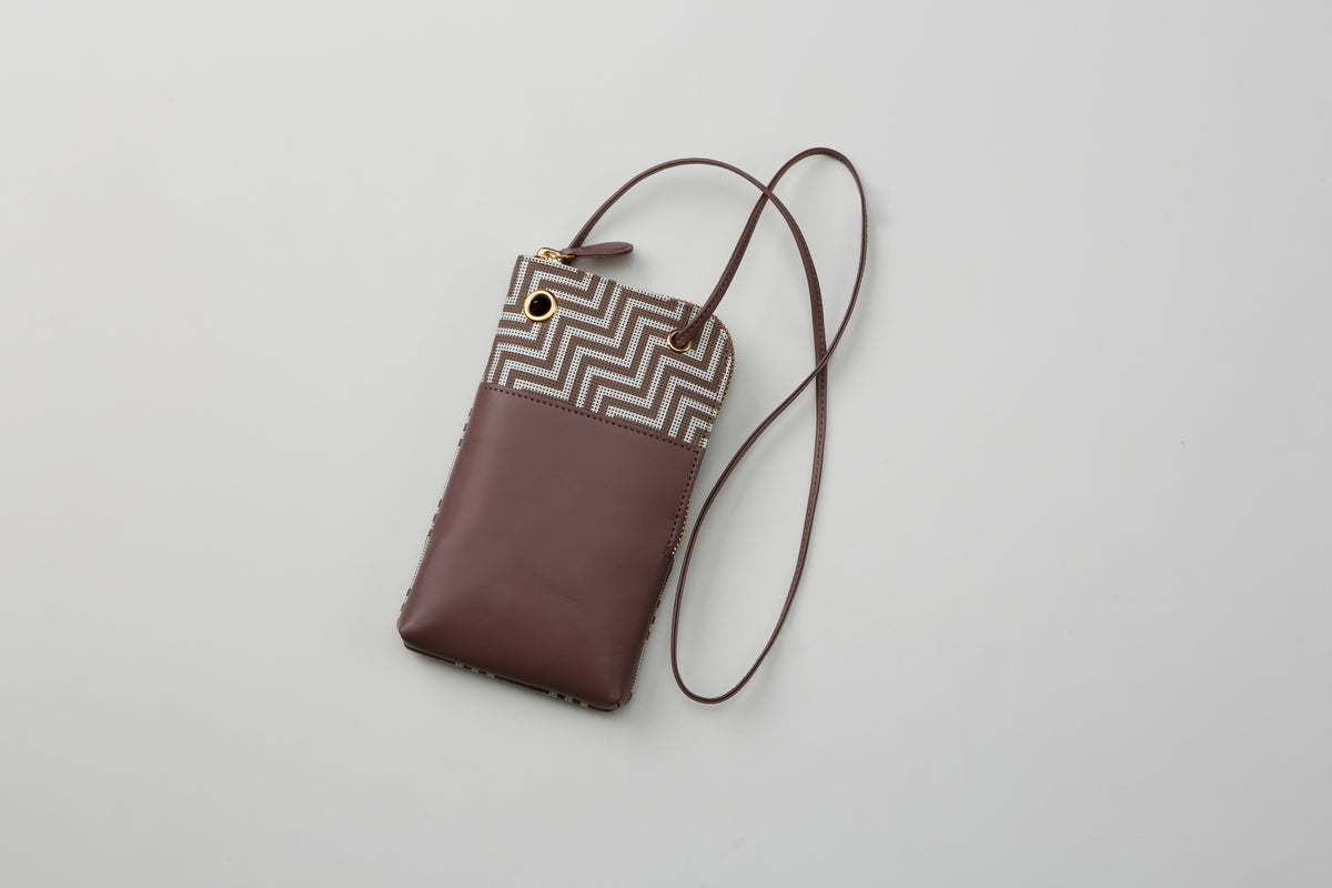 Small rectangular phone case with brown leather bottom and beige and brown geometric chevron pattern top, featuring a thin brown strap attached at the corners.
