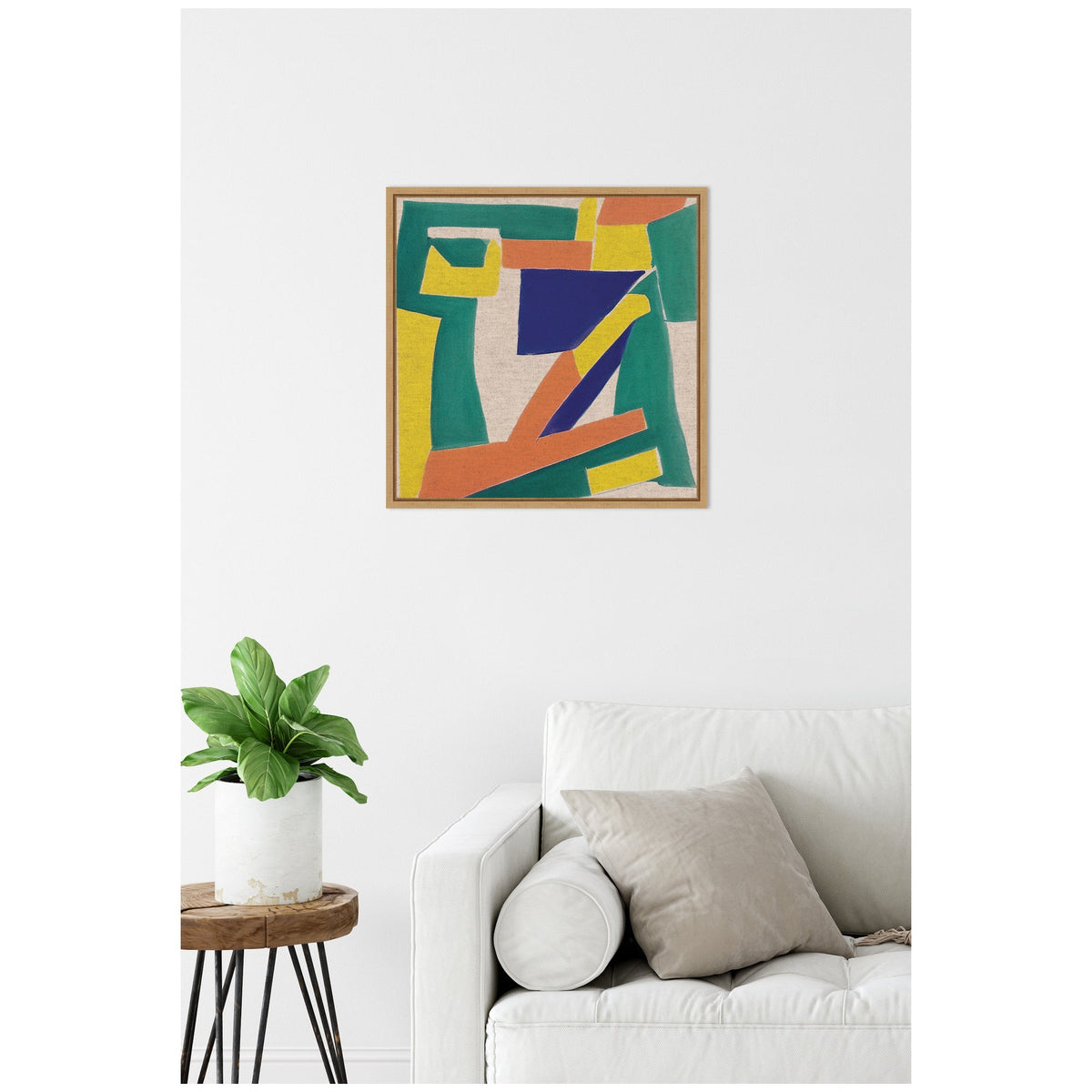 Abstract framed canvas with bold blue, orange, yellow, and green geometric shapes on neutral linen, hanging above a white sofa with beige cushions and a small plant on a round wooden side table.