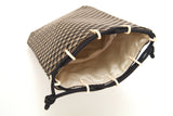 Small drawstring pouch with brown and beige diamond pattern exterior and cream-colored satin interior, featuring black braided drawstrings tied at the ends.