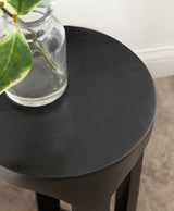 Round black wood drink table with smooth finish, holding a small clear glass vase with a green leaf stem, shown from above in neutral room lighting.