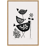 Black linocut print of three stylized birds with patterned bodies perched on and around simple flowers, framed in a light wood frame against white background.